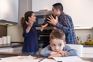 A man and woman argue in the kitchen while a child observes, highlighting the challenge of resolving parental disputes